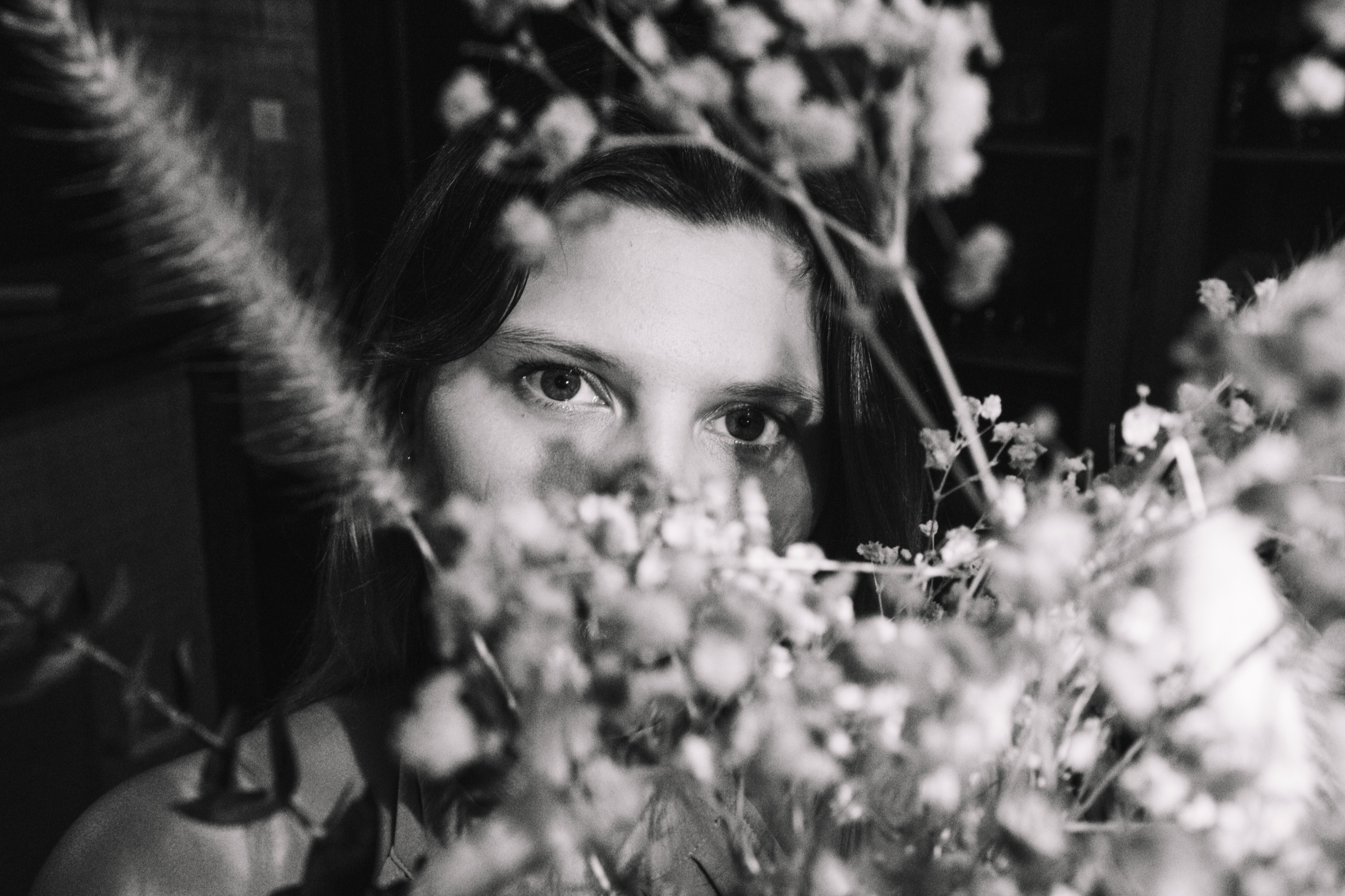 Une femme est photographiée de face, les yeux visibles au-dessus d’un bouquet dense de fleurs qui cache son visage inférieur